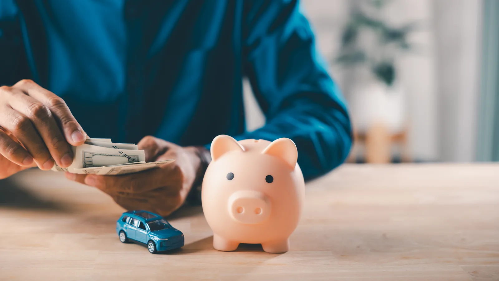 Person counting cash beside a piggy bank and a toy car