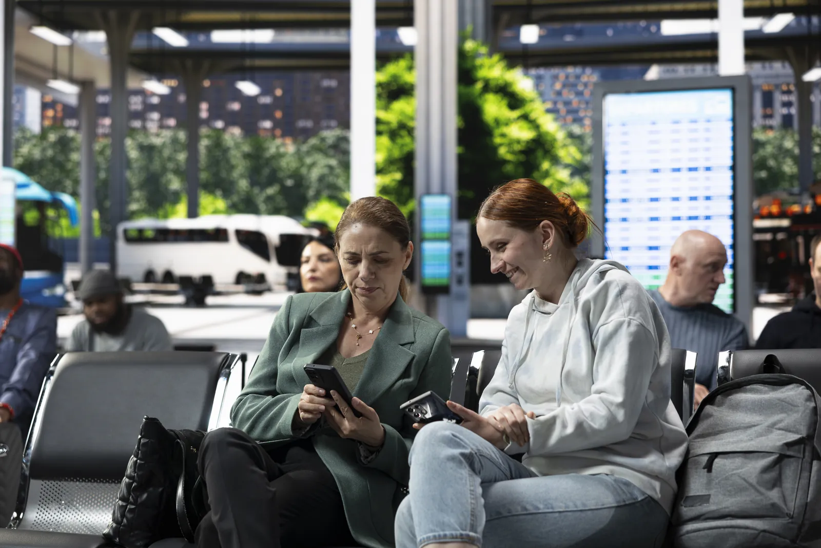 Duas passageiras conferindo seus telefones na sala de espera de um terminal de transporte